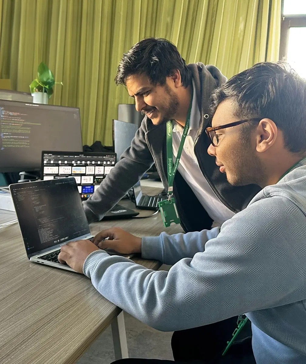 Two DevOps engineers working on a laptop in an office setup.