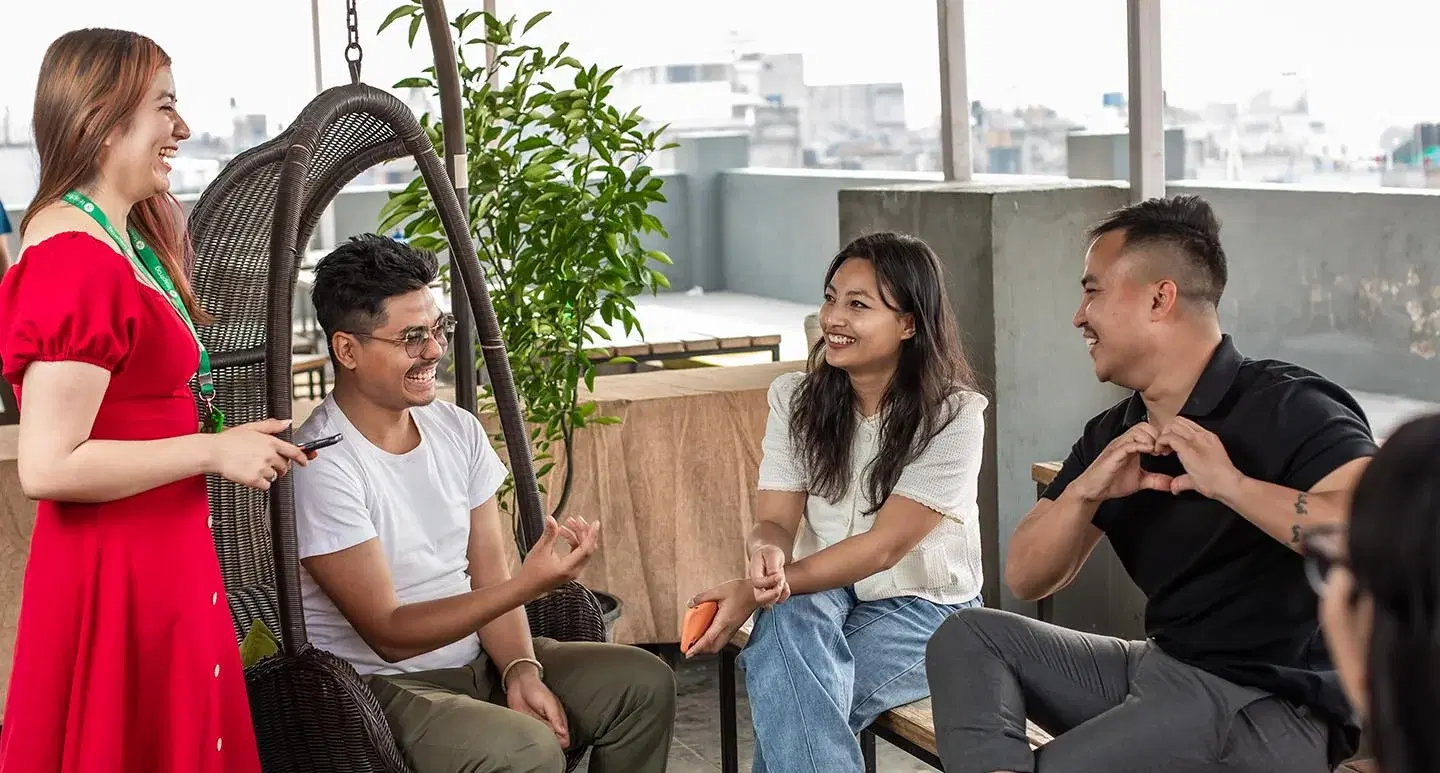 Four employees, one standing and others seated, sharing laughter and enjoyment on a rooftop.