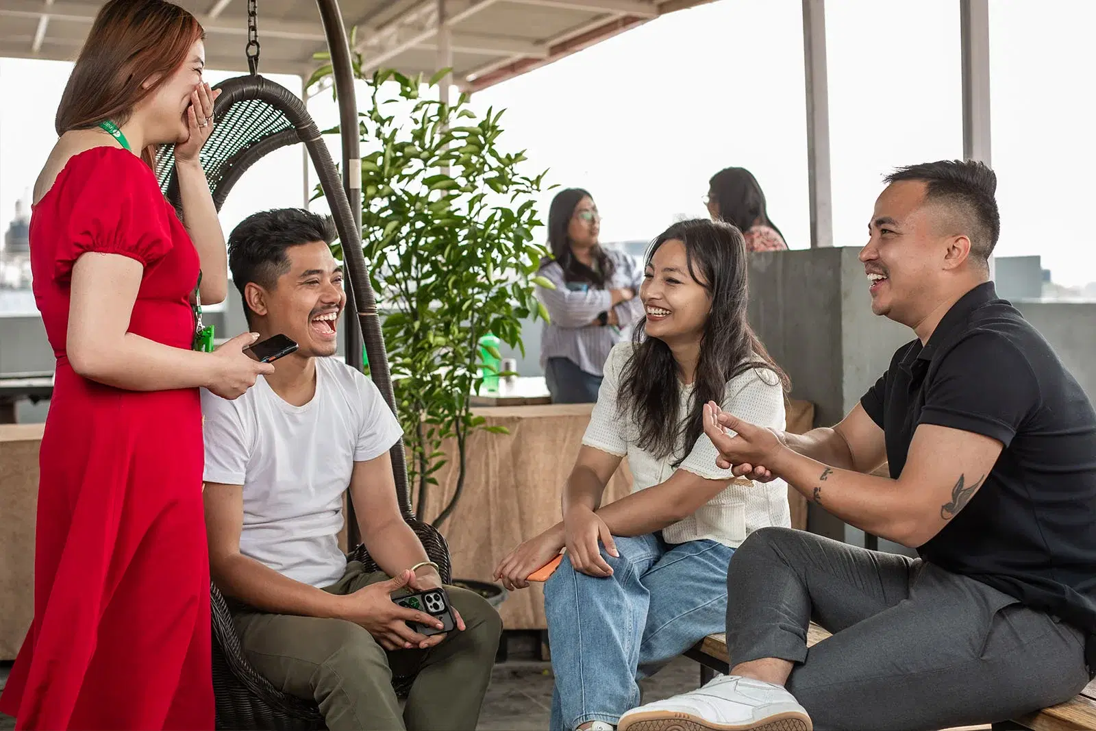 Four employees, one standing and others seated, sharing laughter and enjoyment on a rooftop.